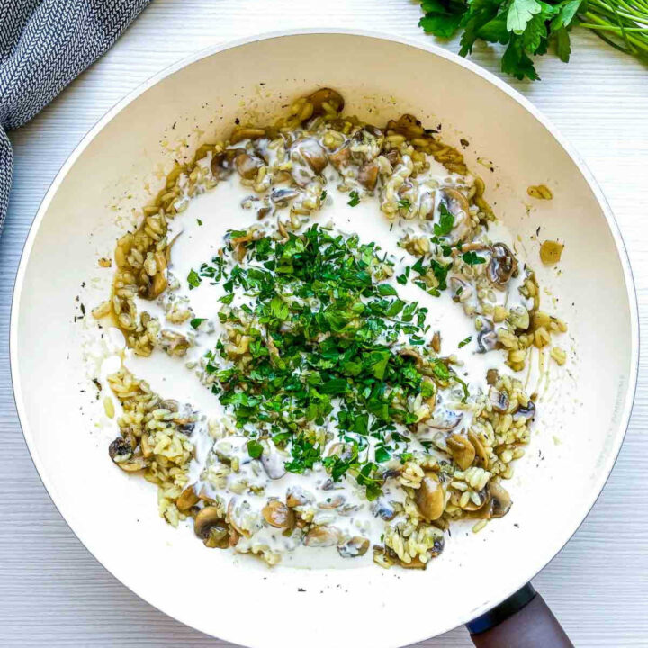 Cream and herbs added to mushroom rice in pan.