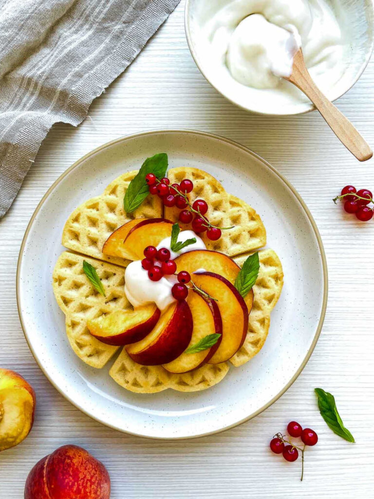Waffles topped with peaches, cream, and red currants