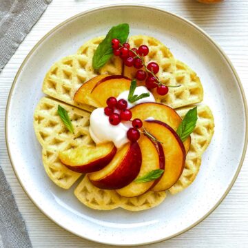 Buttermilk waffles topped with peaches, cream, and red currants