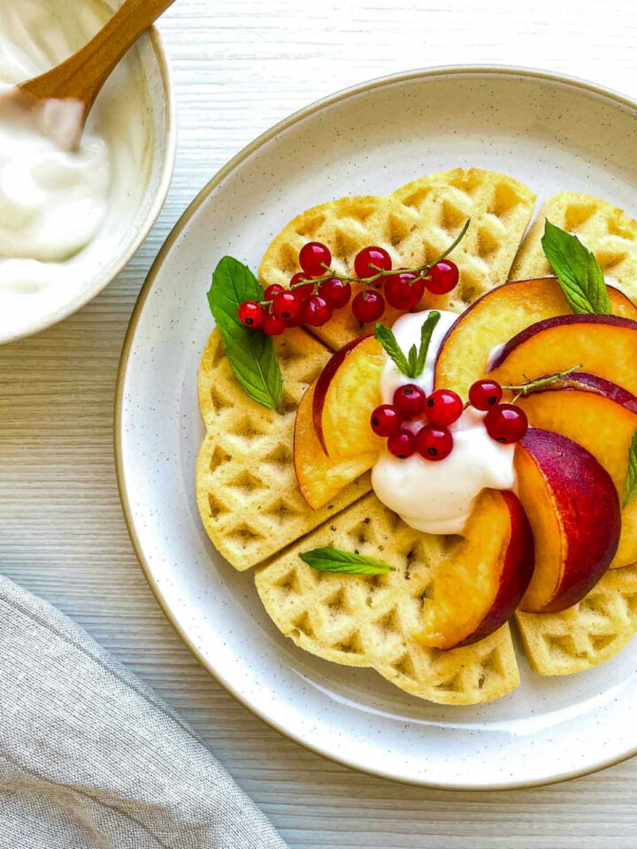 Close up of buttermilk waffles topped with peaches, cream, and red currants