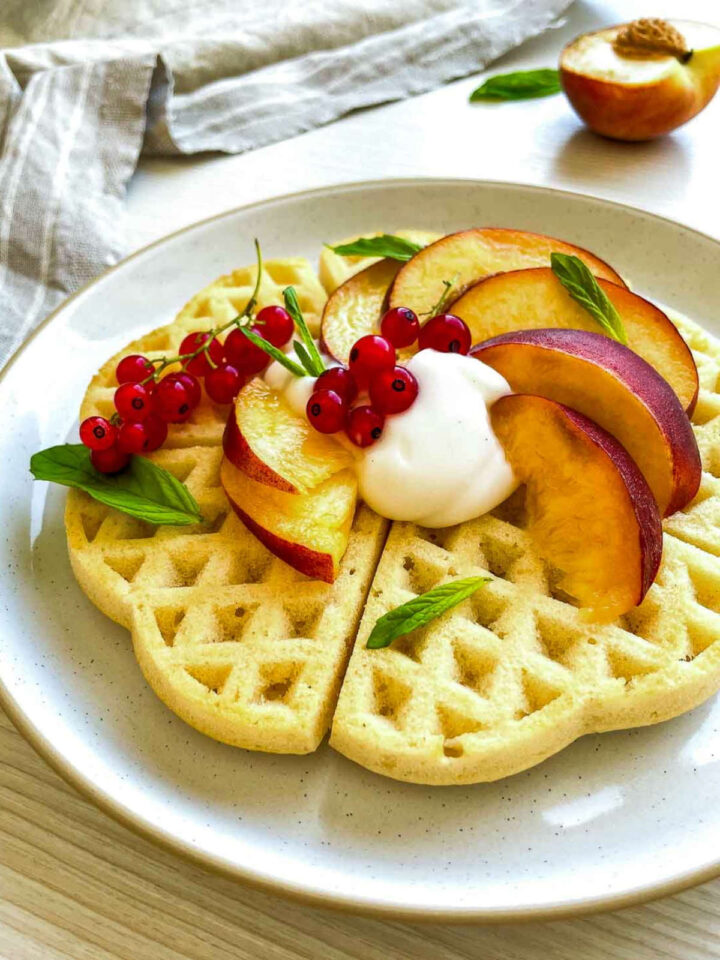 Side view of peach buttermilk waffles served on a white plate.