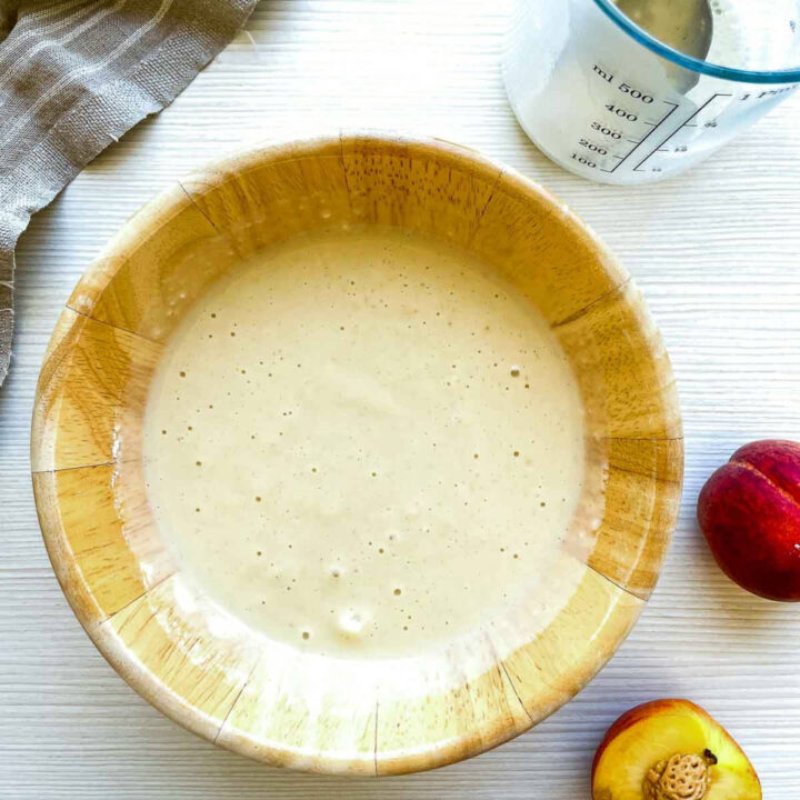 Buttermilk waffle batter in a wooden bowl with peaches nearby