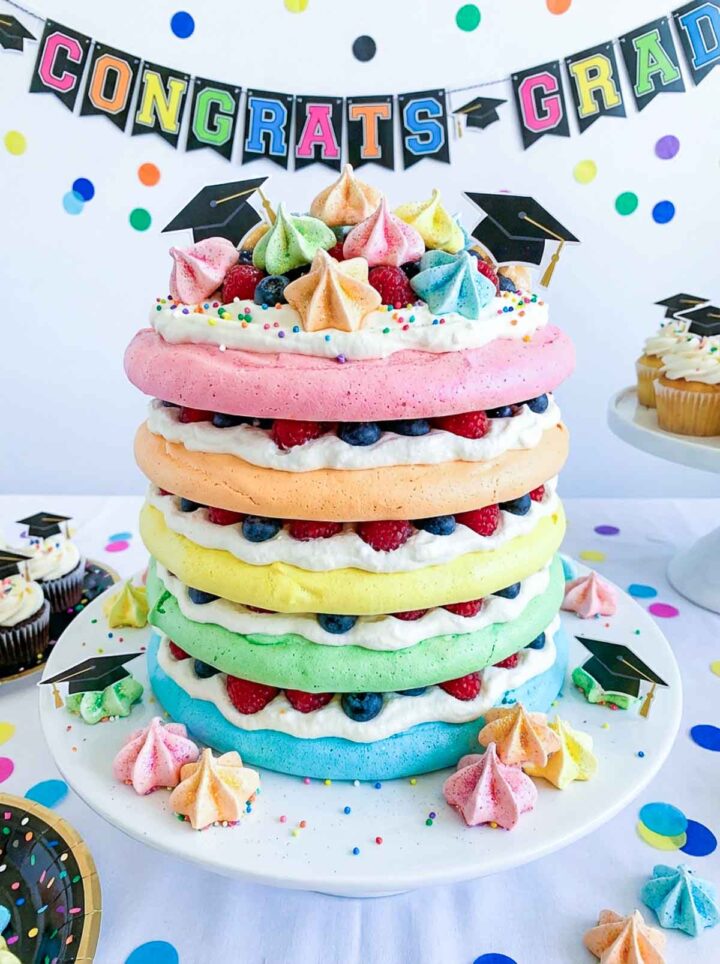 A talk stack of rainbow colored pavlova decorated with berries and meringue bites.