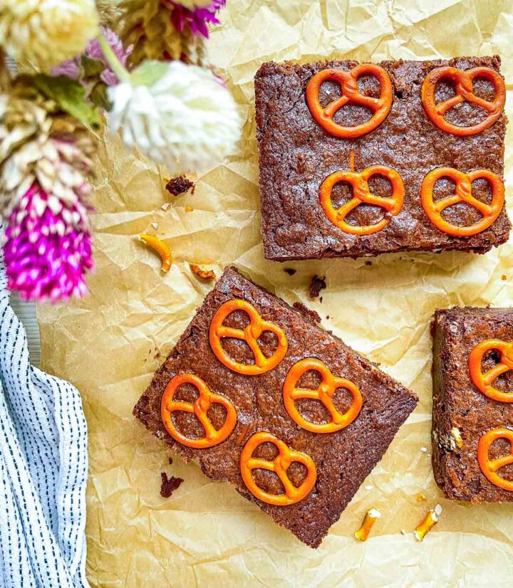 Chocolate brownies topped with mini pretzels on parchment paper