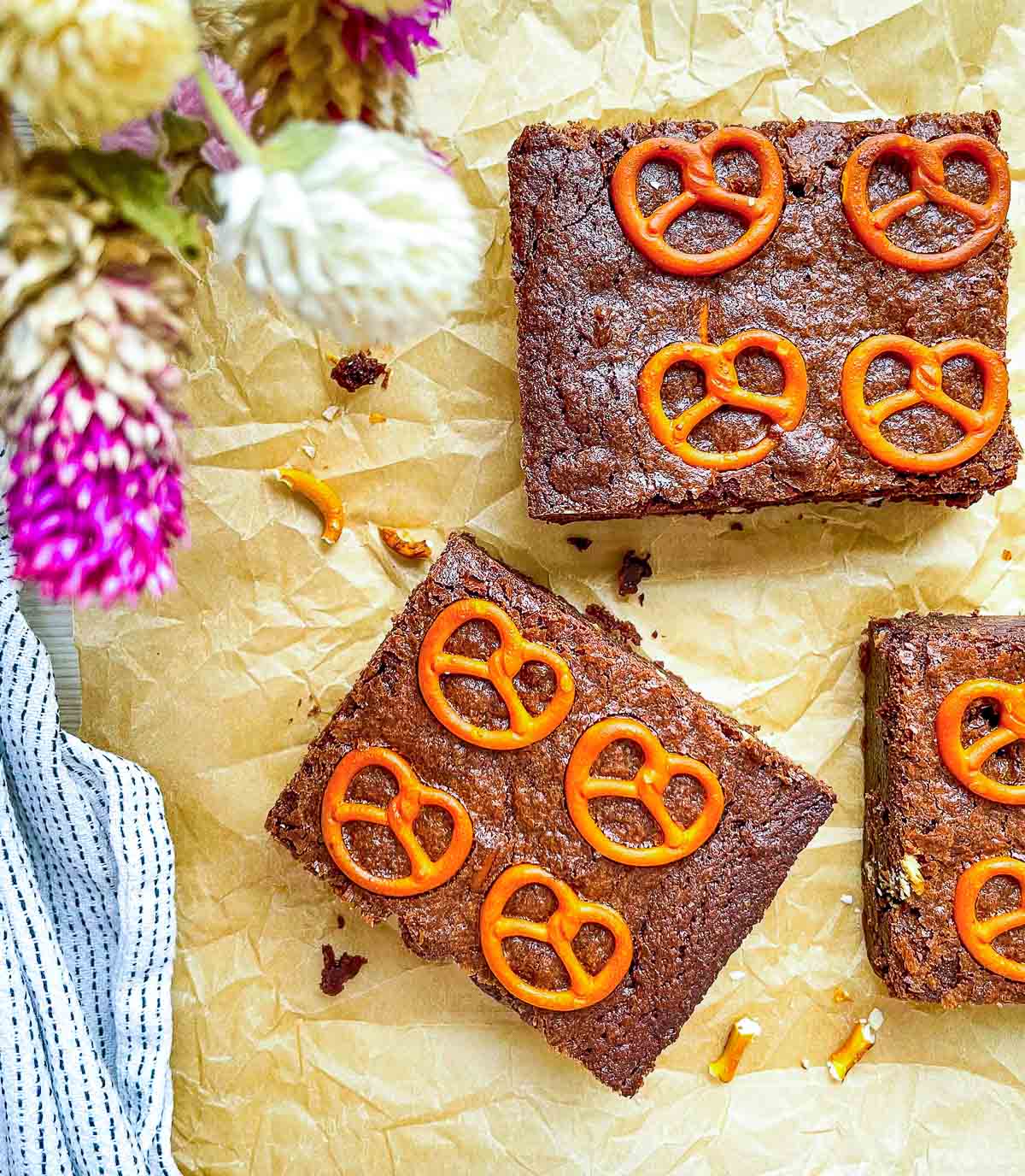 Chocolate brownies topped with mini pretzels on parchment paper