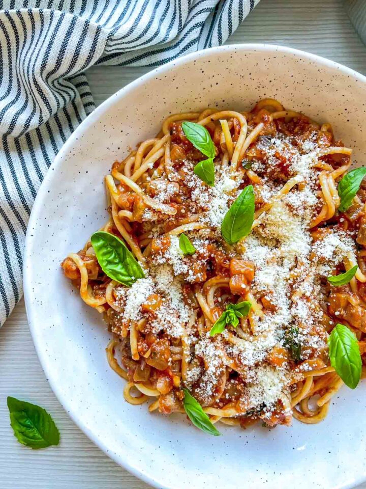 Close-up of spaghetti in a hearty tomato and eggplant sauce, topped with grated parmesan and fresh basil.