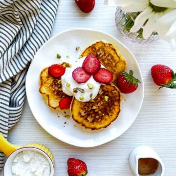 Pancakes topped with strawberries, yogurt, and pistachios