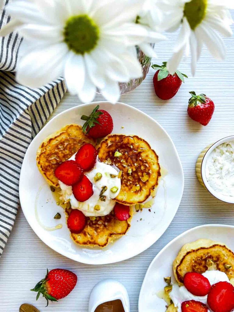 Pancakes with strawberries, yogurt, and pistachios on white plate