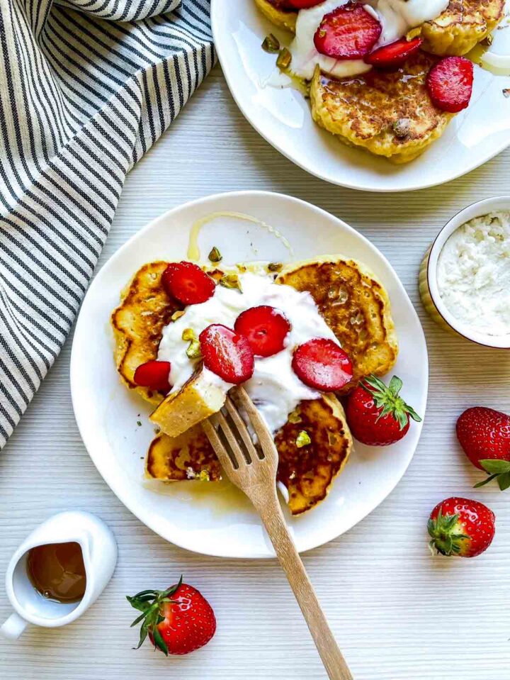 A piece of pancake on a fork held over the plate.