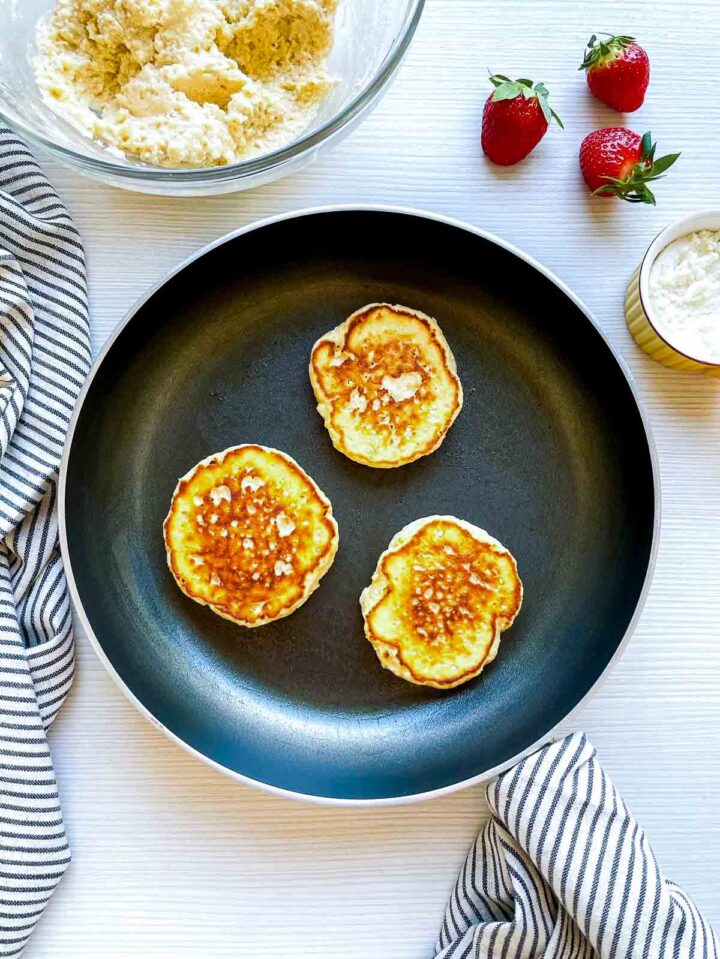 Golden ricotta cheese pancakes cooking in skillet.