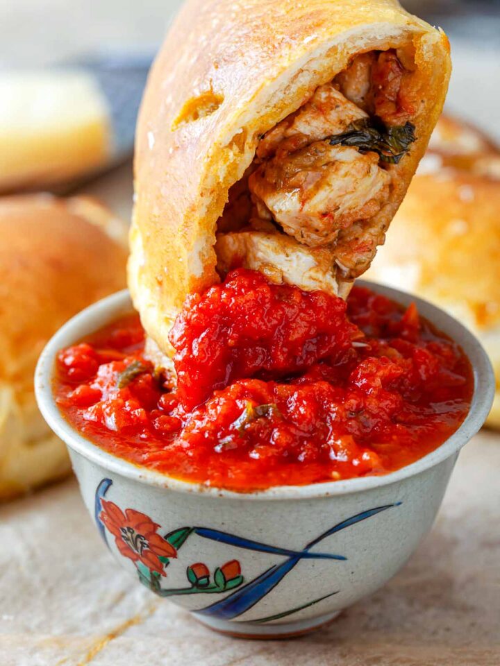 Close-up of a chicken pesto calzone dipped into chunky marinara sauce, showing the tender chicken filling inside.