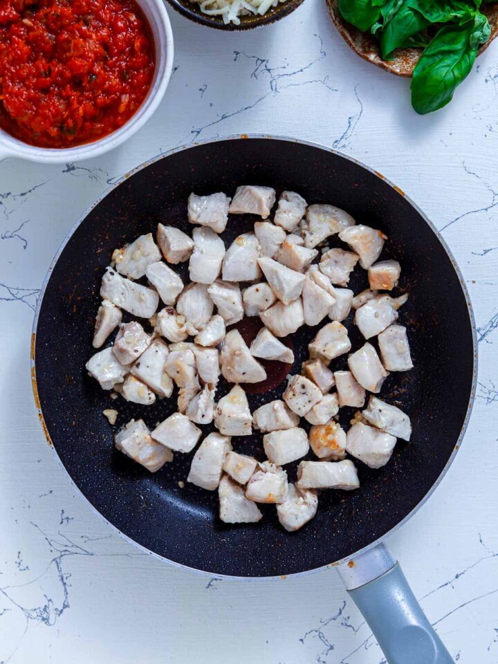 Cubed chicken breast cooking in a skillet with garlic for the chicken pesto calzone filling.