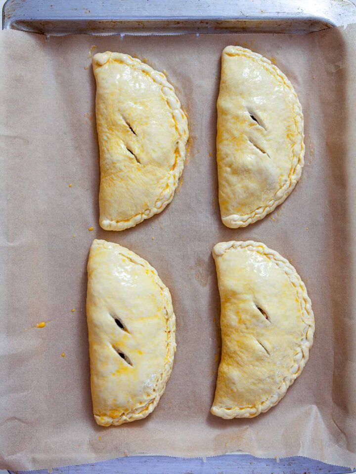 Unbaked chicken pesto calzones brushed with egg wash and arranged on a parchment-lined baking sheet.