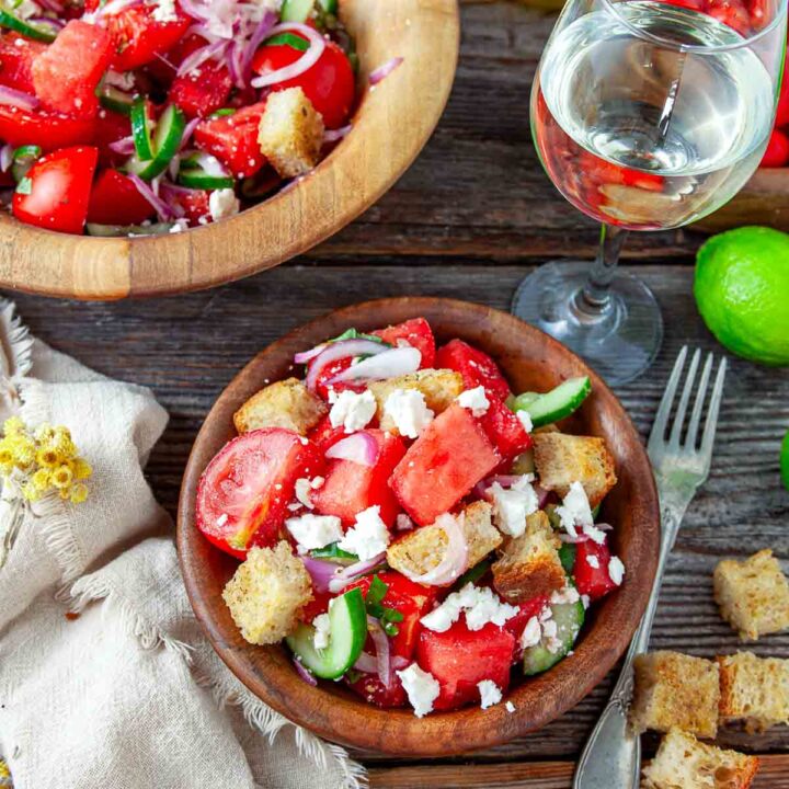 Close overhead view of watermelon tomato panzanella salad in a wooden bowl with red onion, cucumber, feta, and toasted ciabatta croutons.