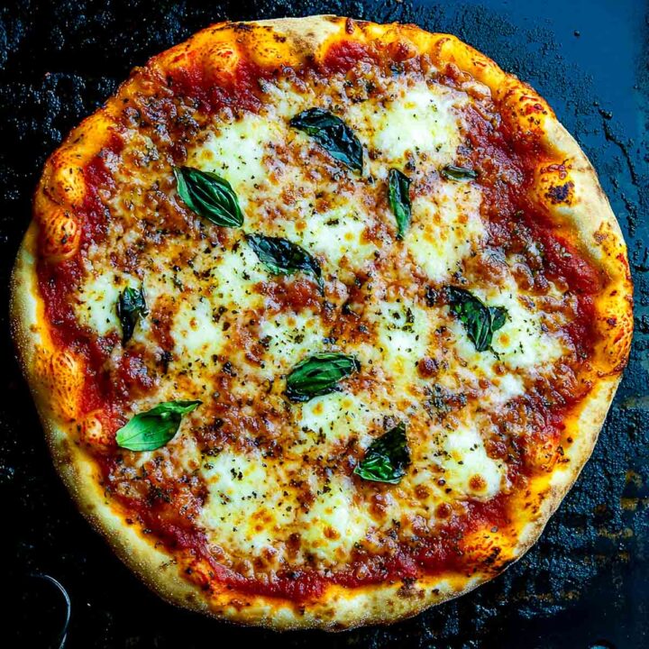 Top-down view of a crispy Blackstone camping pizza with melted mozzarella, rich tomato sauce, and fresh basil leaves cooked on a seasoned flat-top griddle.