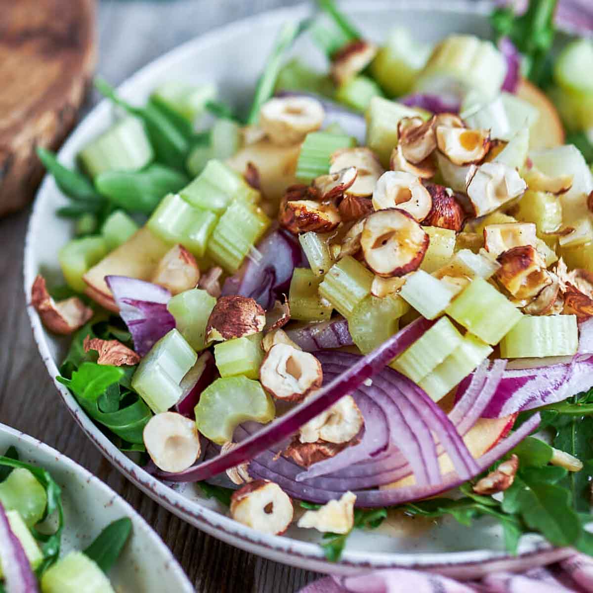 Close-up of arugula, celery, red onion, and chopped hazelnuts drizzled with vinaigrette on a ceramic plate