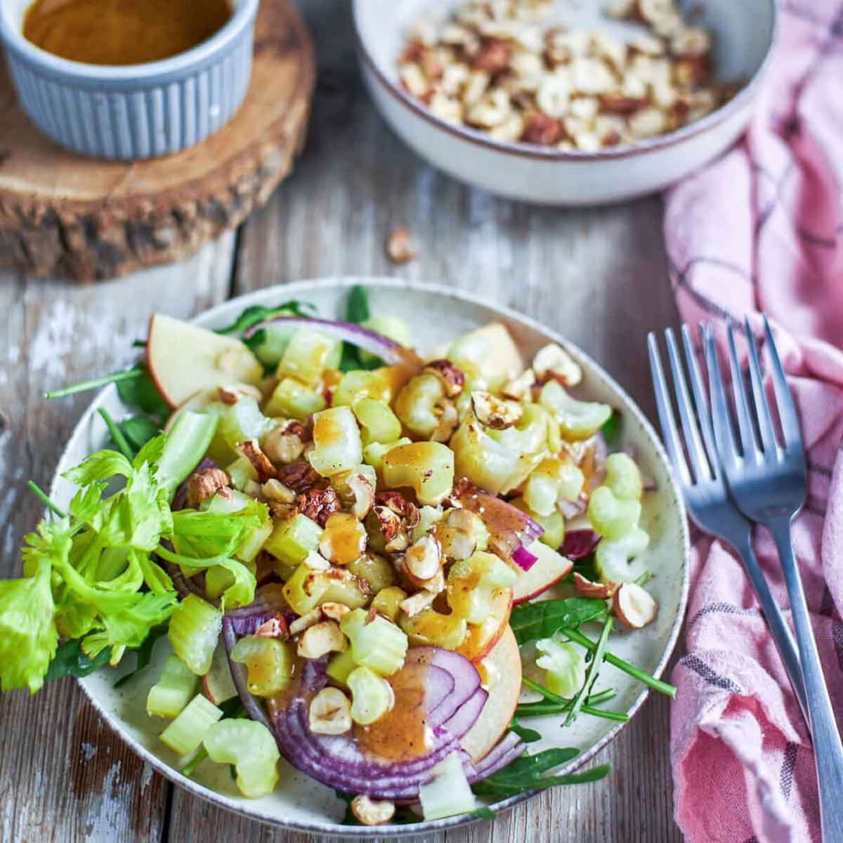 Plated salad drizzled with honey-Dijon vinaigrette, ready to toss, with a bowl of chopped hazelnuts in the background.