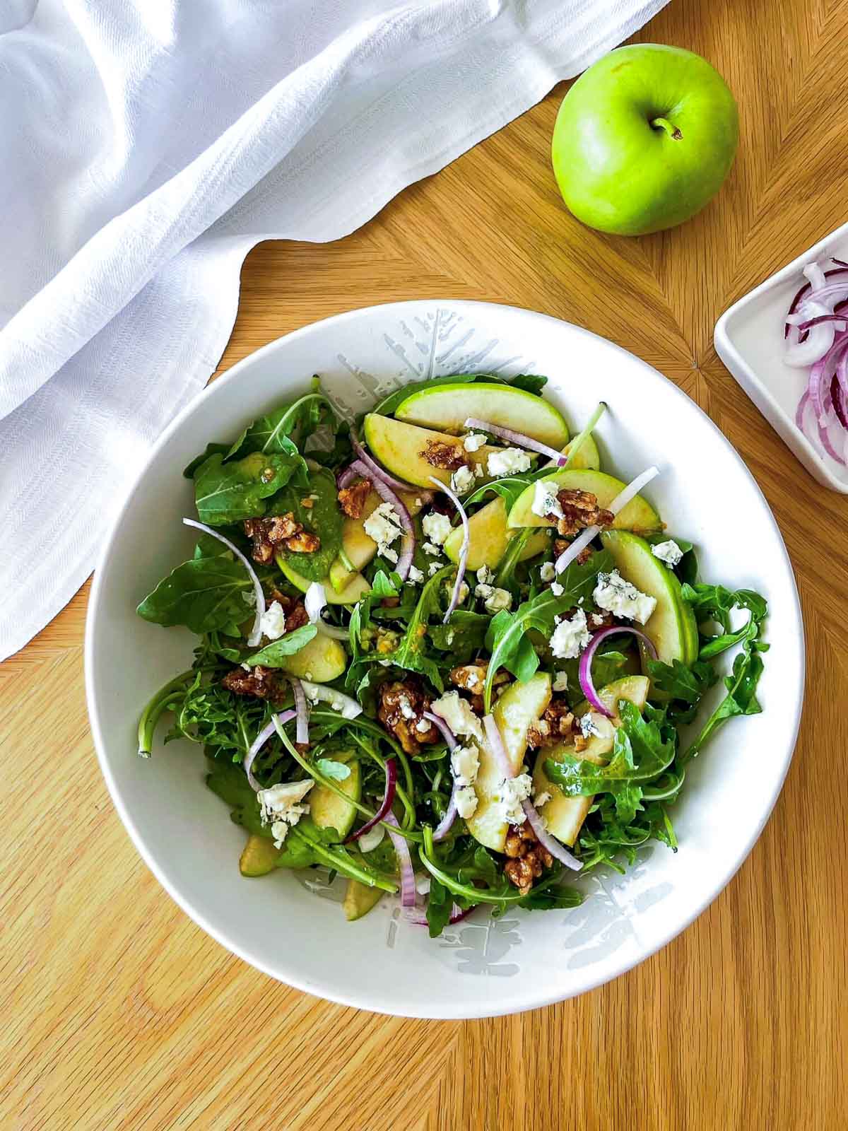Finished apple walnut salad tossed together in a white bowl, ready to serve.
