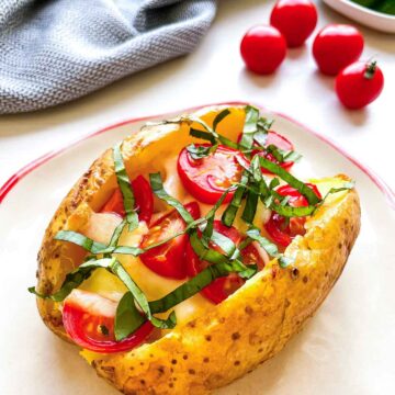 Caprese baked potato topped with melted mozzarella, cherry tomatoes, and fresh basil on a plate.