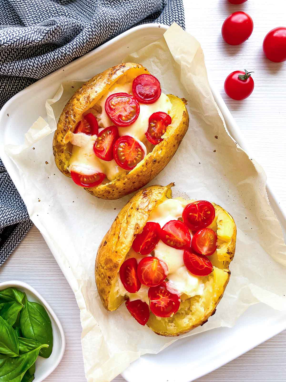 Two potato halves after a second bake, mozzarella melted over marinara and cherry tomatoes, basil not yet added.