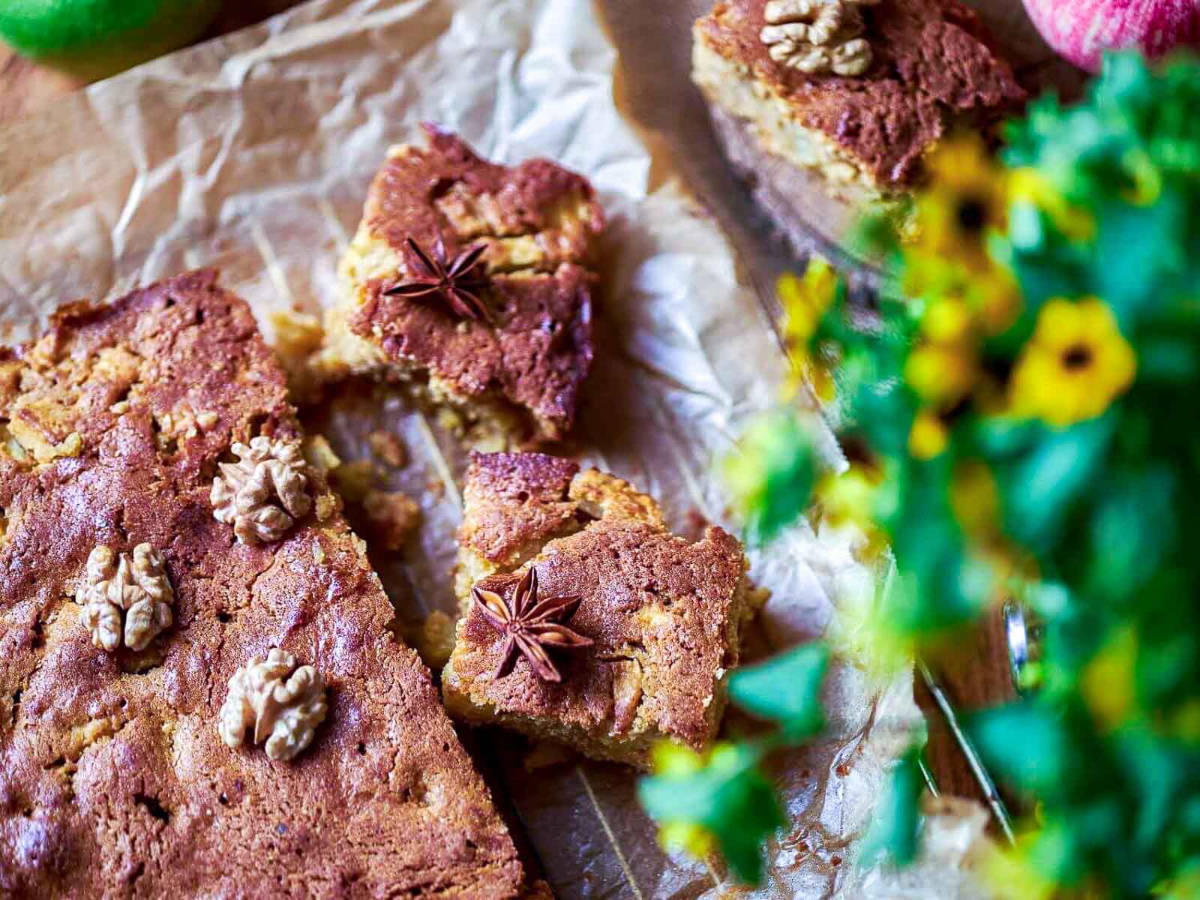 Overhead close-up of cut blondie squares garnished with walnut halves and star anise, with yellow flowers in the foreground.