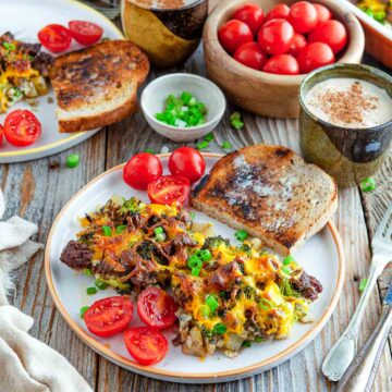 Potato sausage broccoli breakfast casserole topped with melted cheddar and green onions, served with toast and fresh tomatoes.