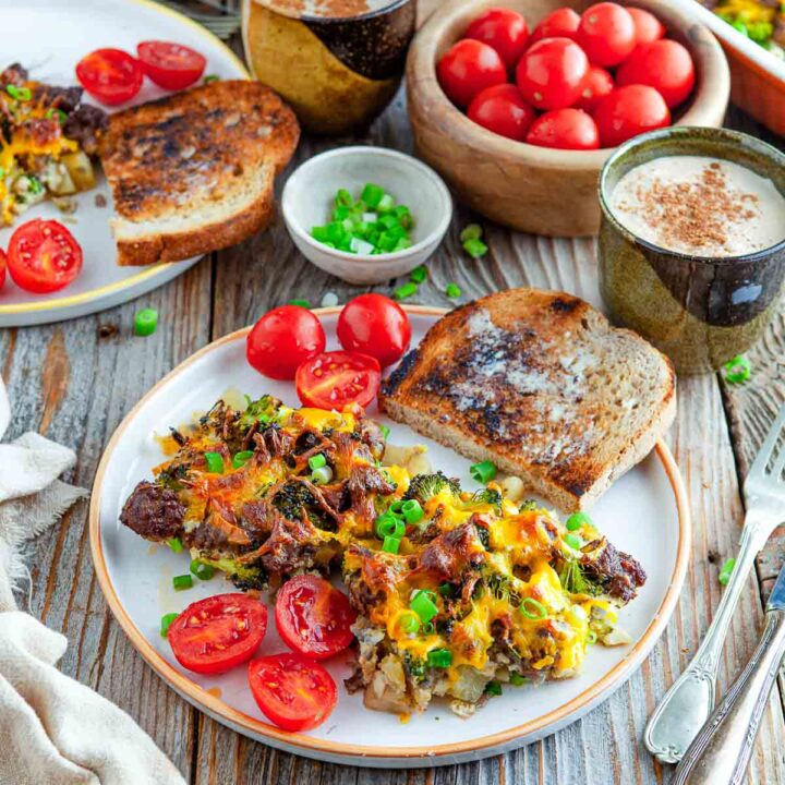 Potato sausage broccoli breakfast casserole topped with melted cheddar and green onions, served with toast and fresh tomatoes.