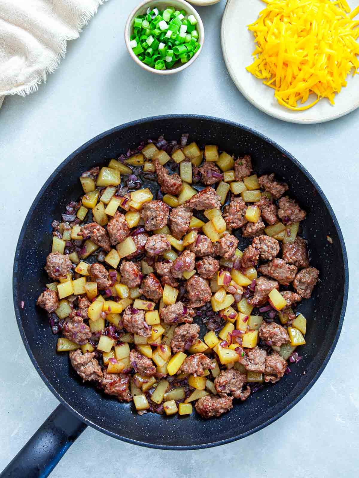 Browned Italian sausage, diced potato, and red onion cooking together in a skillet.
