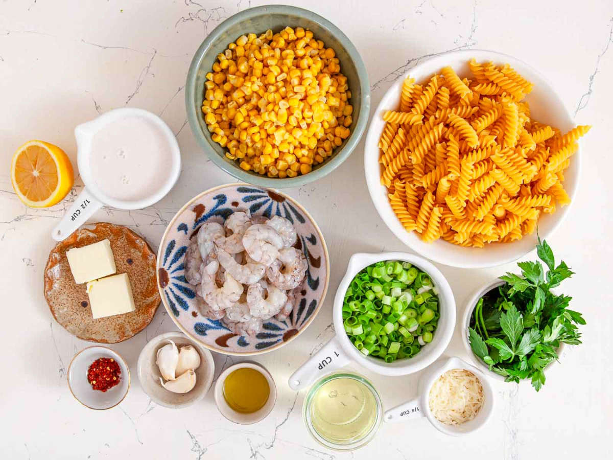 Ingredients laid out for the recipe, including rotini pasta, raw shrimp, corn kernels, butter, garlic, scallions, parsley, lemon, olive oil, chili flakes, and parmesan.