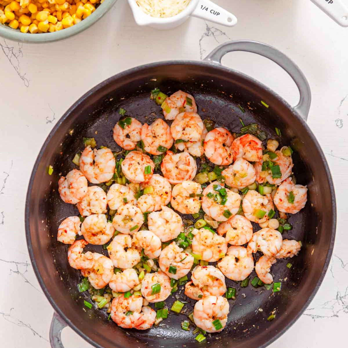 Cooked shrimp with sliced scallions and red chili flakes in a skillet.