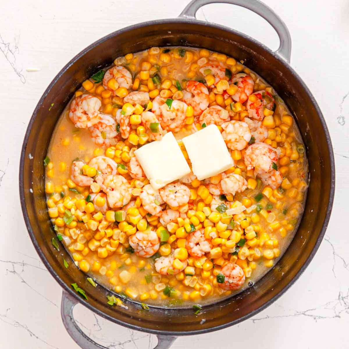 Corn and shrimp simmering in a skillet with two pats of butter melting on top.