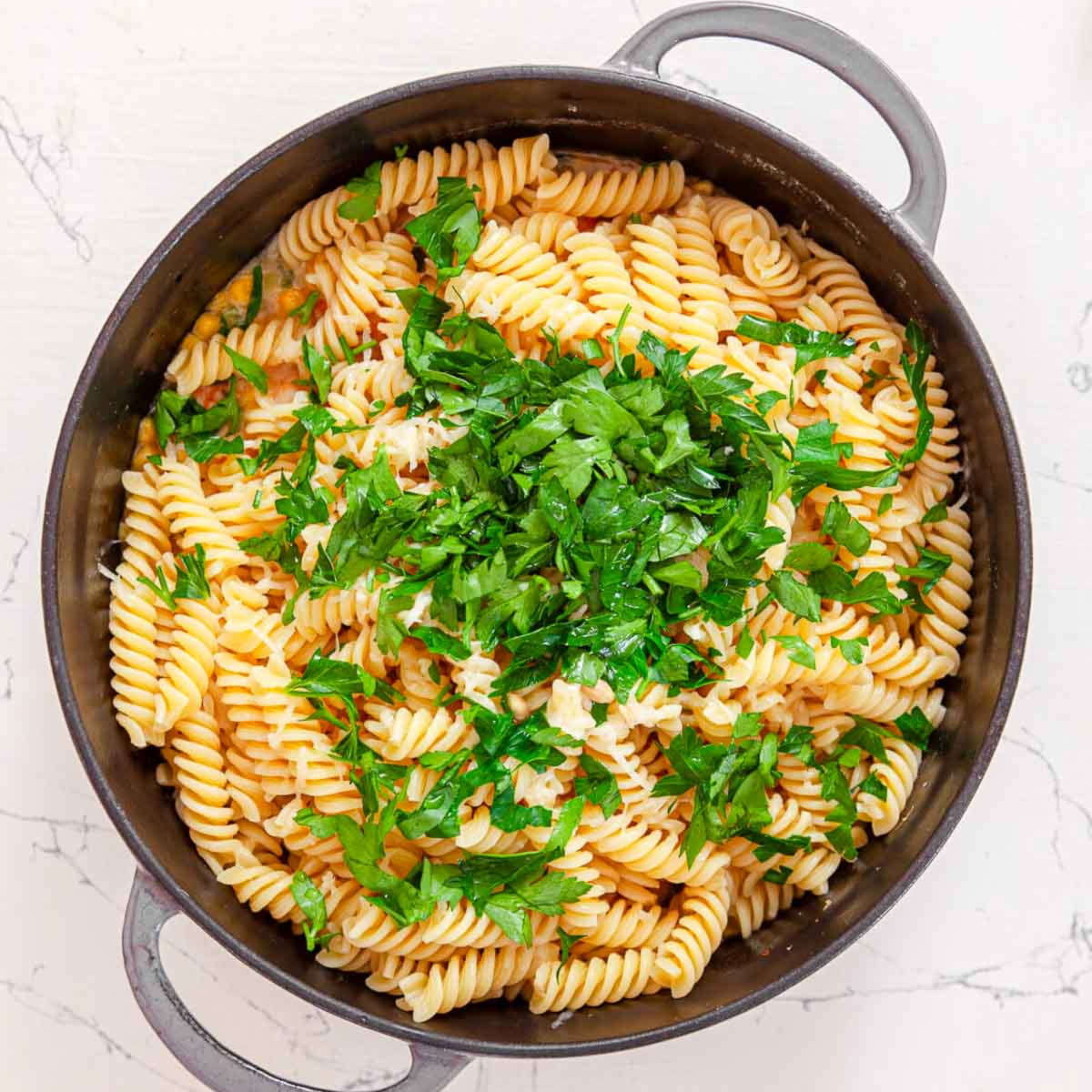 Cooked rotini topped with a pile of chopped parsley in a skillet, ready to be tossed with the shrimp and corn.