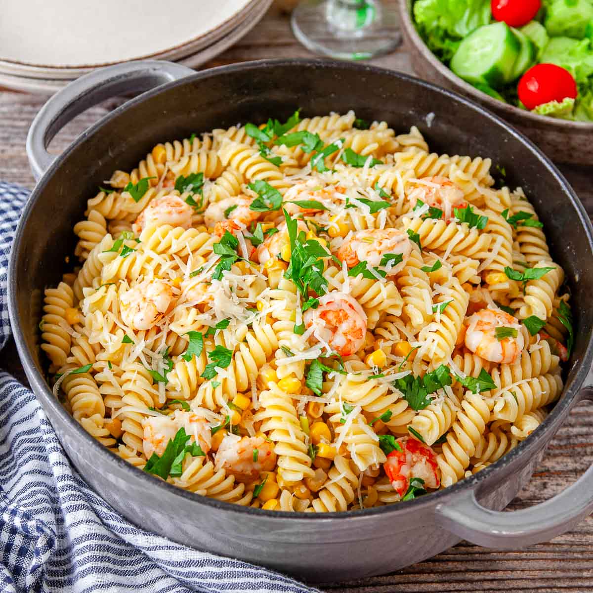 Finished skillet of shrimp and corn rotini garnished with parsley and grated parmesan.