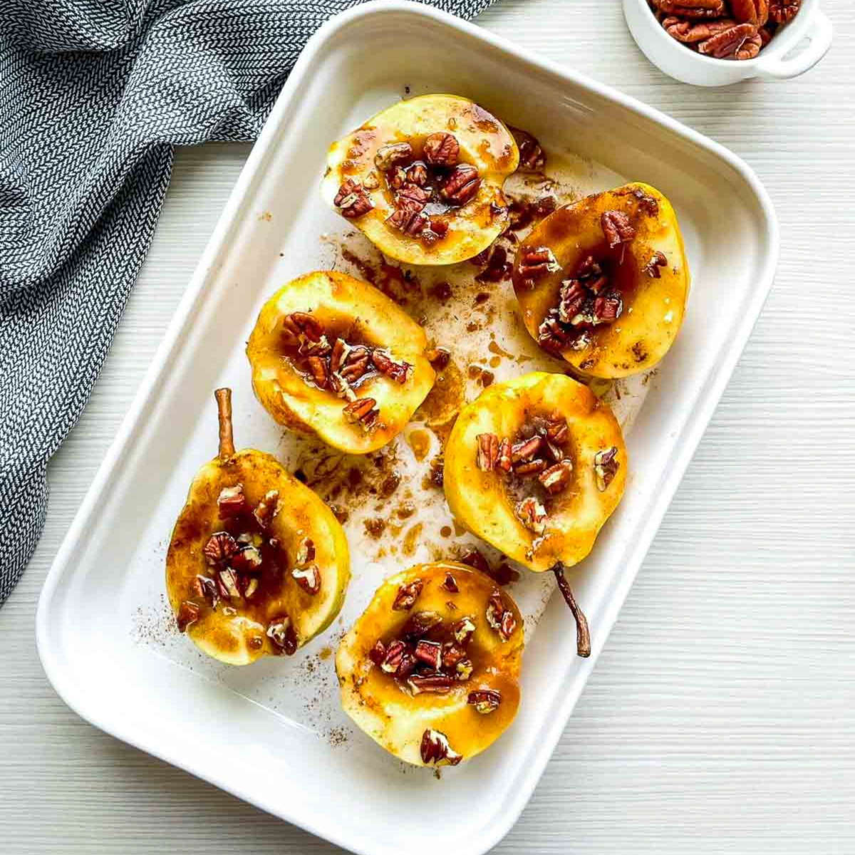 Pear halves coated in a light-colored oil and spice mixture, arranged cut-side up in a white baking dish, not yet baked.