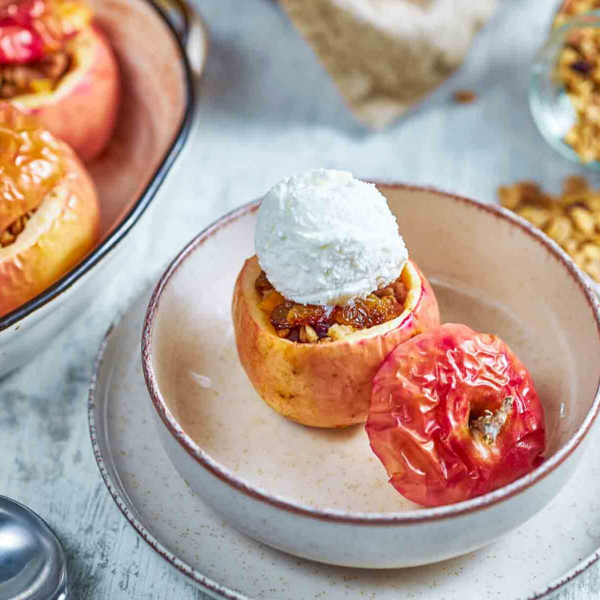 a granola stuffed baked apple topped with vanilla ice cream, with additional baked apples blurred in the background