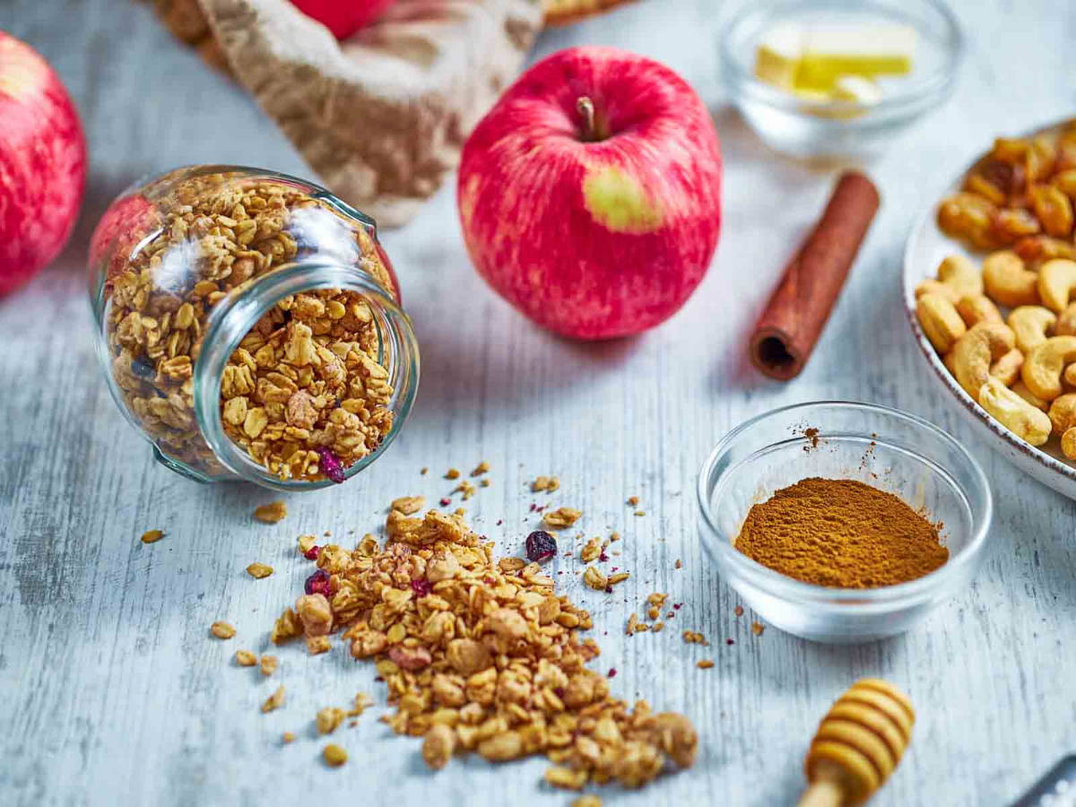 granola, a whole apple, cinnamon, butter, and cashews arranged on a wooden surface