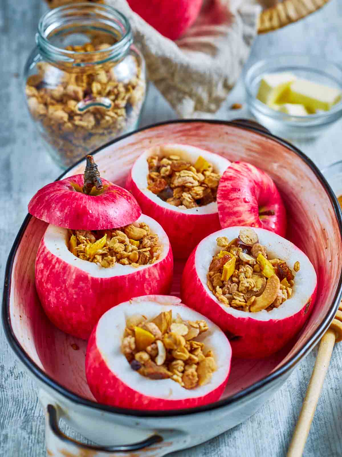  four hollowed apples filled with granola mixture, arranged in a ceramic baking dish with the apple tops set to one side
