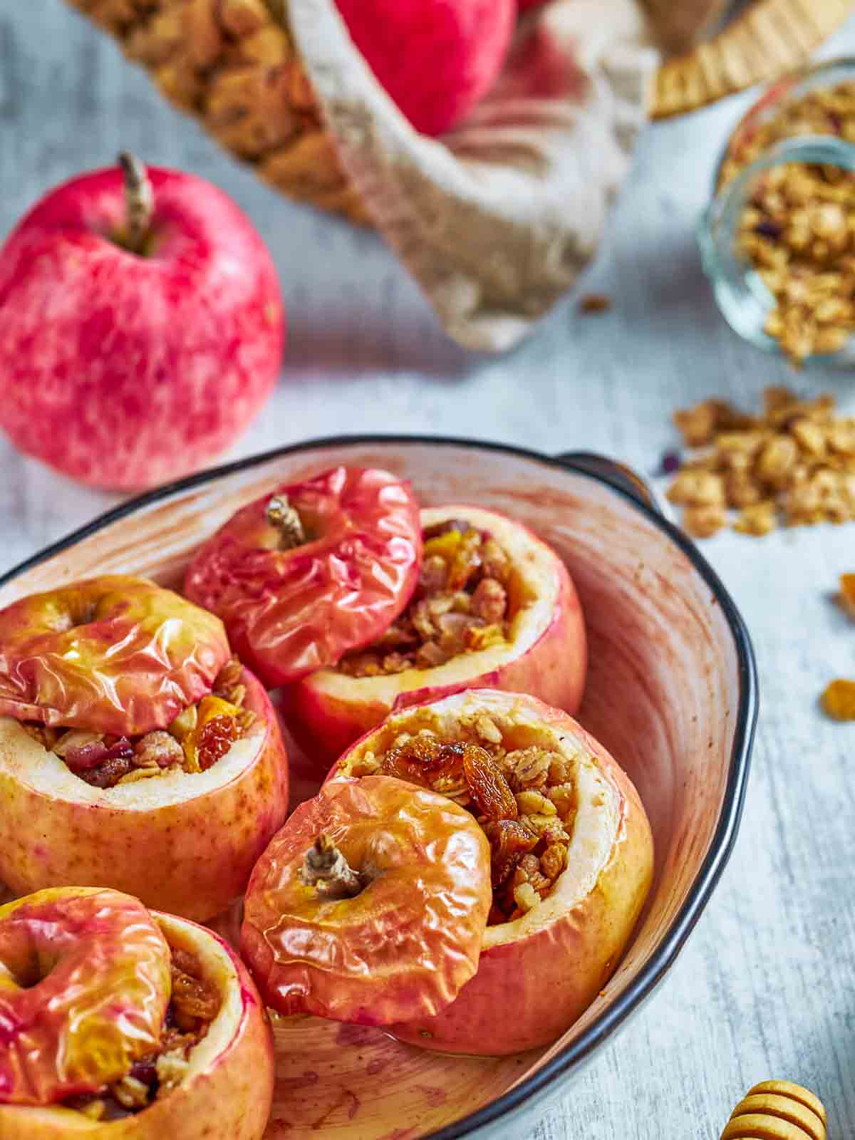baked apples with softened, shriveled skins and caramelized granola filling, in a baking dish