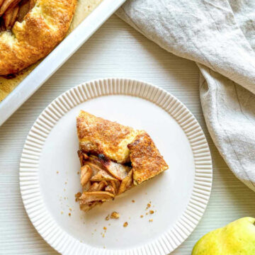 Slice of homemade pear galette with cinnamon-spiced pears and a golden flaky crust served on a white plate.