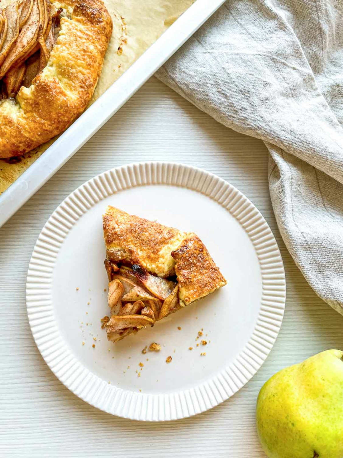 Slice of homemade pear galette with cinnamon-spiced pears and a golden flaky crust served on a white plate.