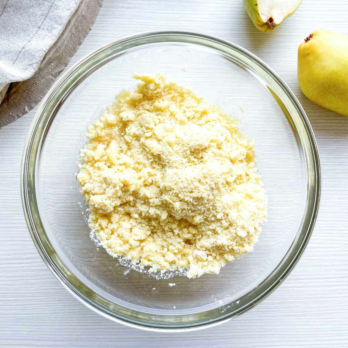 : A glass bowl filled with a crumbly mixture of flour and small pieces of butter, ready to be brought together into pie dough.