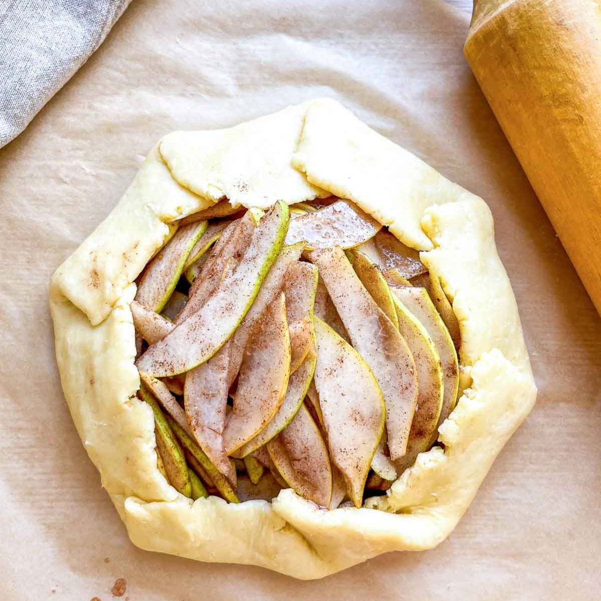 An unbaked galette with the pie dough folded up around the edges of the pear filling, ready to be brushed with egg wash.