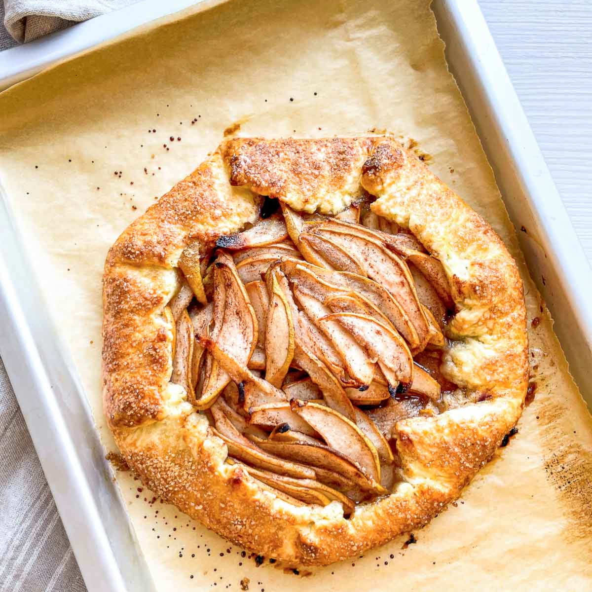 A freshly baked pear galette with a deep golden crust, still on its parchment-lined sheet pan.