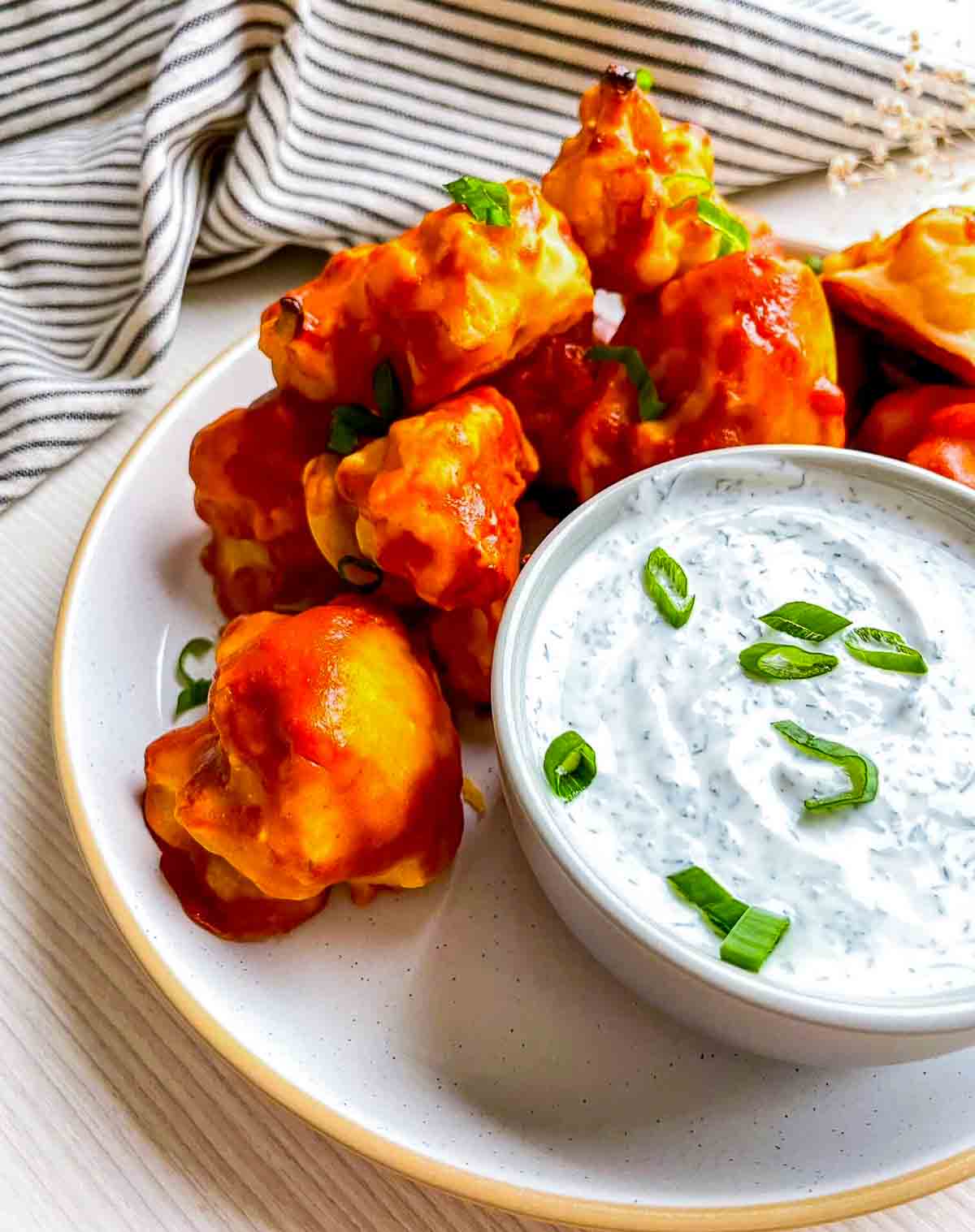 Close view of buffalo cauliflower bites with dip, served on a speckled plate with sliced green onions