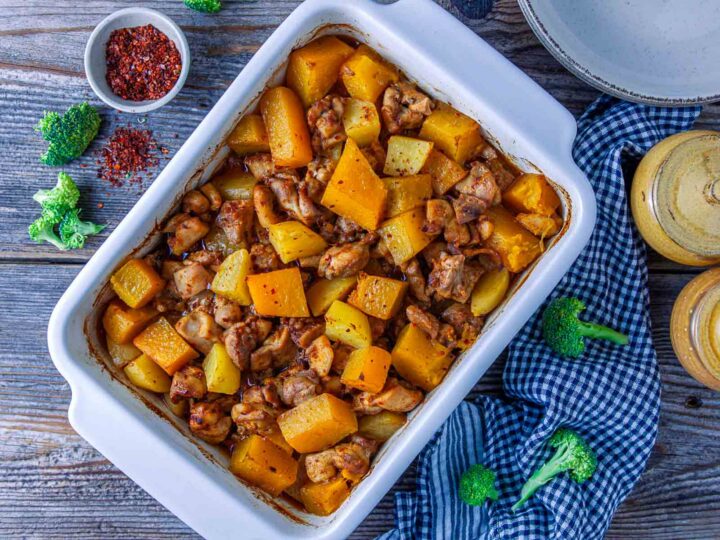 Baked pumpkin chicken casserole with potatoes in a white ceramic dish, garnished with red chili flakes.