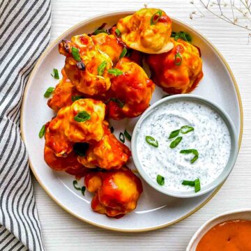 Overhead view of golden orange cauliflower wings beside a bowl of herb dip on a speckled plate