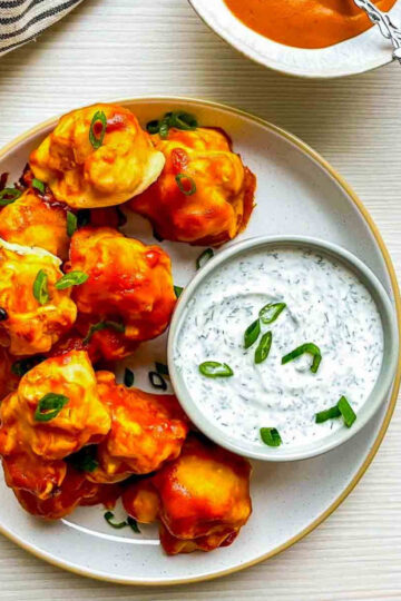 Buffalo cauliflower wings on plate with a bowl of creamy herb dip and scattered green onions
