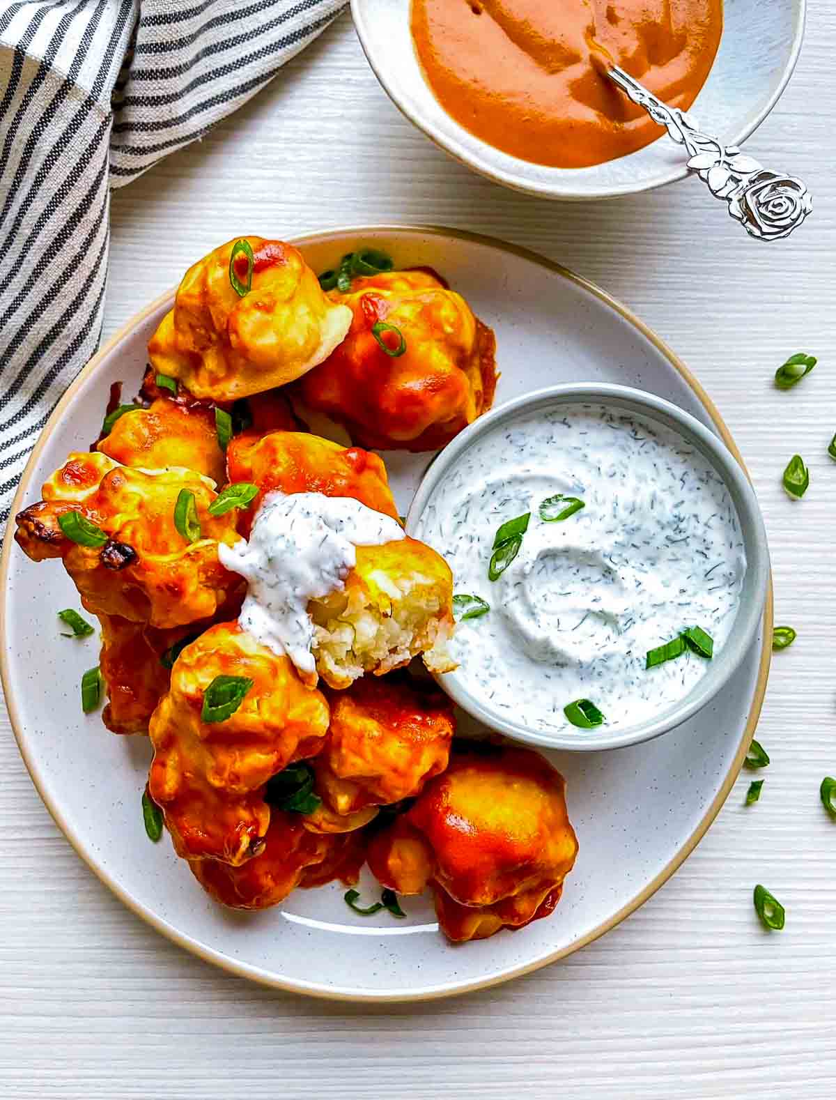 A bitten buffalo-coated cauliflower floret topped with creamy herb dip, showing the tender white center