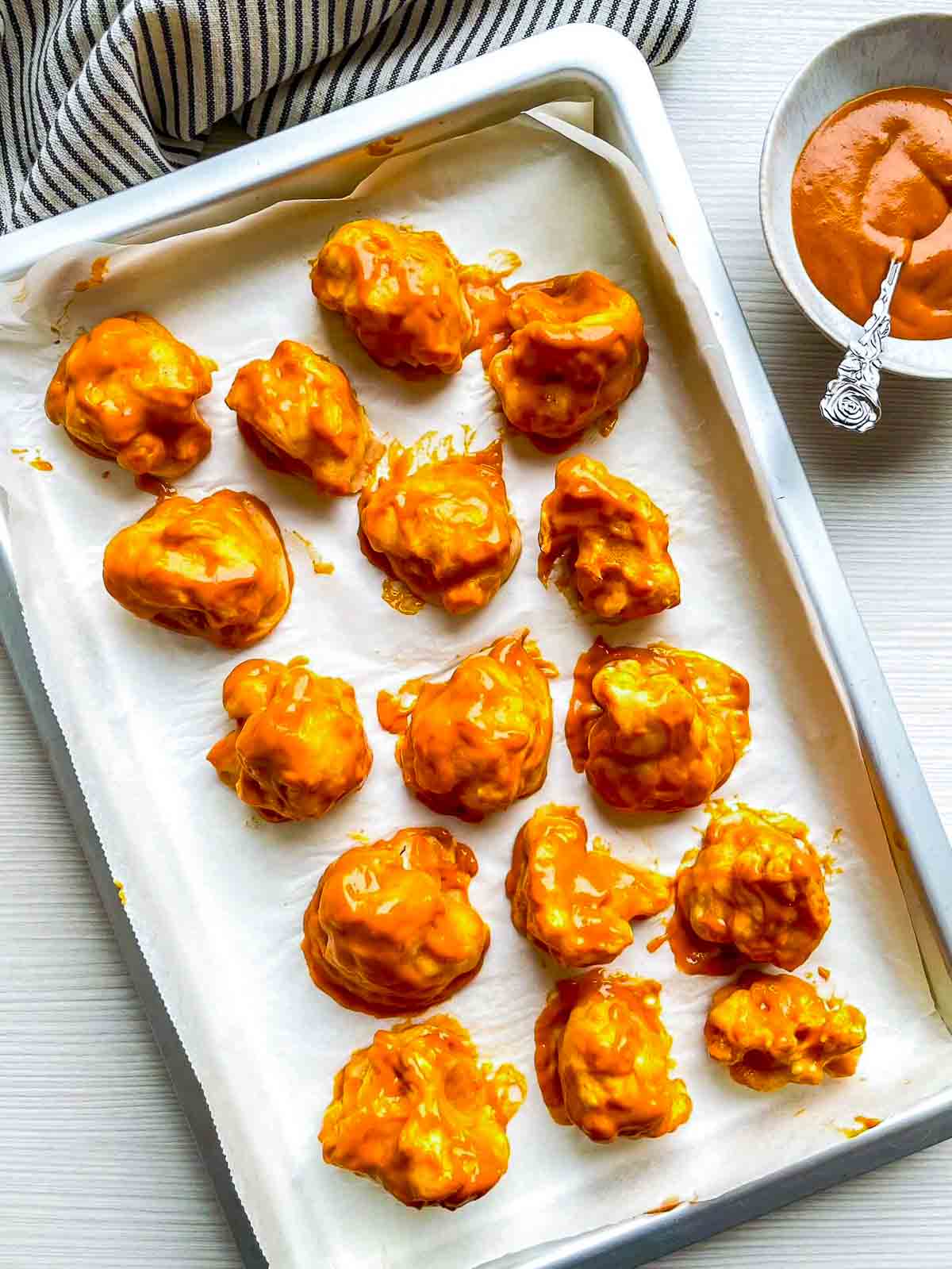 Baked florets coated in glossy orange buffalo sauce on a parchment-lined baking sheet before the second bake