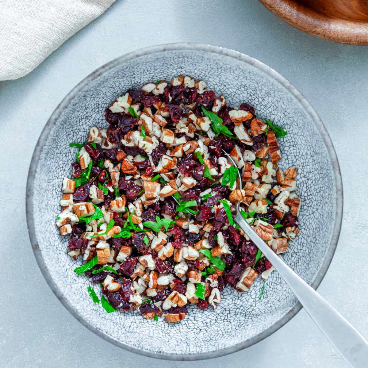 Chopped pecans, dried cranberries, and fresh parsley tossed together in a speckled gray bowl with a spoon